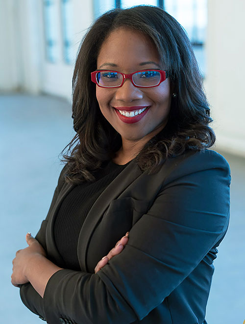 Talithia Williams smiling and standing at an angle to the camera with her arms crossed