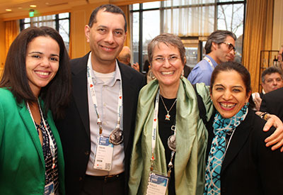 Four previous Forum attendees smiling and looking at the camera with arms around one another